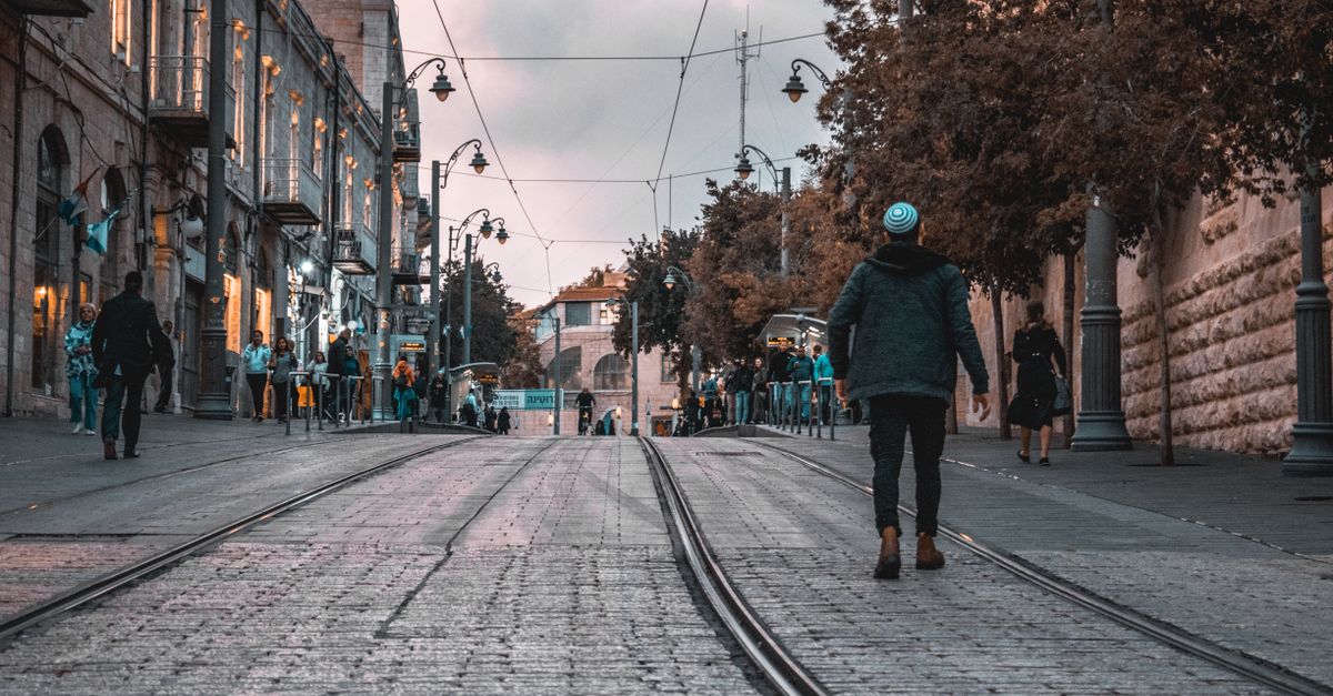 A bustling city street with tram tracks, people walking, and historical buildings at dusk.
